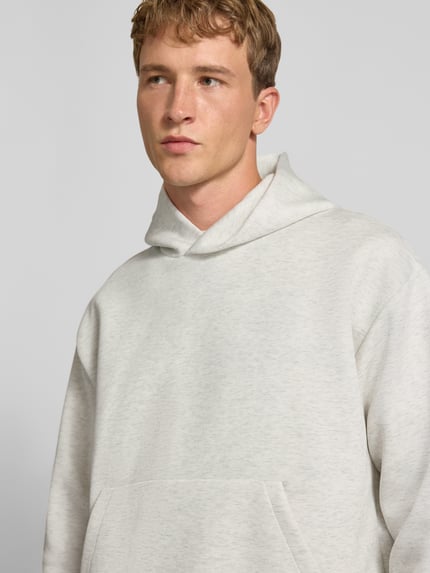 Männermodel trägt Relaxed Fit Hoodie mit Baumwoll-Anteil Modell 'Barron' von JACK & JONES in hellgrau, glatte Textur, Nahaufnahme Oberkörper. Material-Mix, Kapuze, Kängurutasche, elastische Abschlüsse, Rückenlänge 66 cm, Ärmellänge 58 cm.