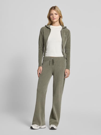 Frauenmodel trägt Sweatjacke mit Kapuze Modell 'MAYA KNIT HOODIE' von Juicy Couture in unifarbener Strickoptik, Cropped-Länge, Logo-Stitching, Reißverschluss, Kapuze, langarm, gerippte Abschlüsse, Ganzkörperansicht von vorne.