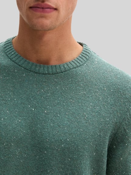 Männermodel trägt Pullover mit Logo-Detail von MARC O’POLO in melierter Strickoptik, grün, Struktur-Muster, Nahaufnahme Oberkörper.