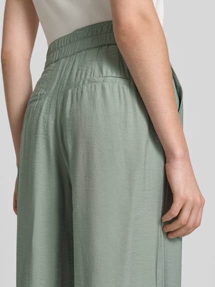 Frauenmodel trägt Wide Fit Chino aus Viskose-Mix mit Gesäßtaschen von Betty Barclay in hellem Grün, feine Struktur, Detailaufnahme Rückansicht, Damen Chino, Haken- und Reißverschluss, Bundweite 36 cm, Innenbeinlänge 80 cm, Größe 36.