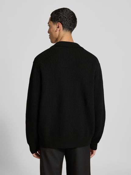 Männermodel trägt Cardigan aus reiner Wolle von Filippa K in Schwarz, lockere Passform, Ripp-Optik, Rückansicht, Ganzkörperansicht.