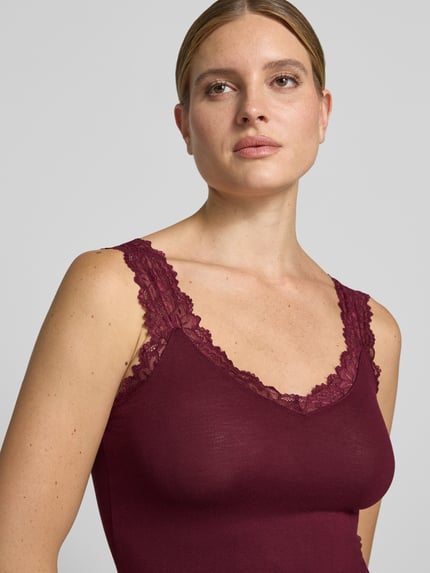 Frauenmodel trägt Slim Fit Tanktop aus Viskose-Mix Modell 'ROSA' von VERO MODA in Dunkelrot mit Spitzenbesatz, Nahaufnahme Oberkörper. Damen Tanktop von VERO MODA