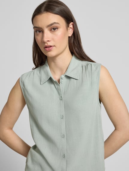 Frauenmodel trägt Regular Fit Leinenbluse ohne Ärmel Modell 'SIESTA' von Only in Melange-Optik aus Viskose-Leinen-Mix mit Hemdblusenkragen, einreihiger Knopfleiste und Raffungen, Nahaufnahme Oberkörper.