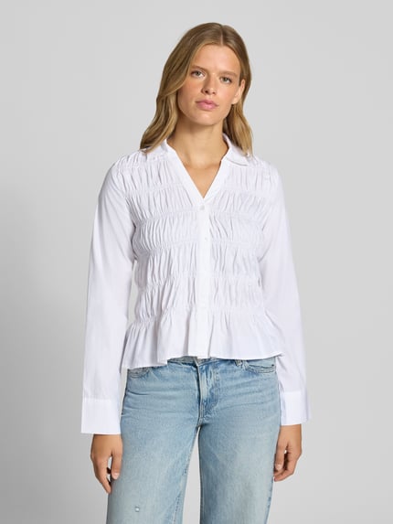 Frauenmodel trägt Slim Fit Bluse mit Smok-Details von Gina Tricot in Weiß, Hemdblusenkragen, V-Ausschnitt, reine Baumwolle, Ganzkörperansicht von vorne.