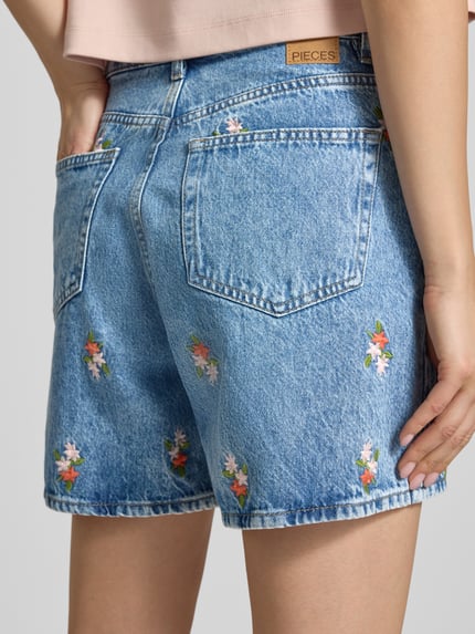 Frauenmodel trägt Regular Fit Jeansshorts aus reiner Baumwolle Modell 'SKY' von Pieces, Denim-Optik, Stickerei, Nieten, 5-Pocket-Design, Ganzkörperansicht Rückansicht.