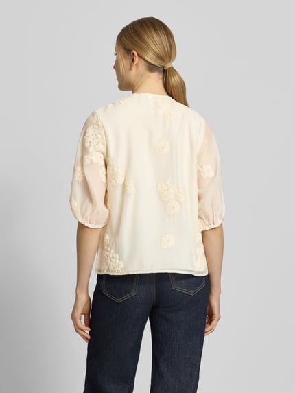 Frauenmodel trägt Regular Fit Bluse mit floralem Zierbesatz von Jake*s Collection aus leichtem Baumwoll-Mix in Creme, Rückenansicht, Ganzkörperansicht Rückansicht. Rundhalsausschnitt mit Zier-Bordüre, Halbarm mit elastischen Ärmelabschlüssen und durchgängiger Knopfleiste, Rückenlänge bei Größe 36: 58 cm, Ärmellänge: 34 cm.