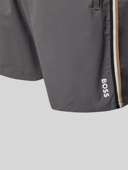 Mannenmodel draagt Badehose met elastische tailleband Modell 'ICONIC' van BOSS, effen met labelprint en contraststreep, detailopname.