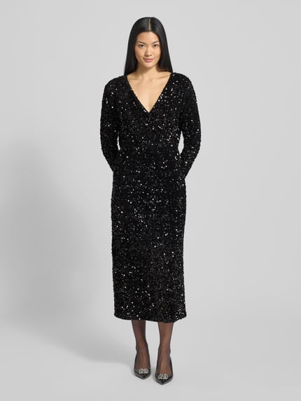 Frauenmodel trägt Midikleid mit V-Ausschnitt Modell 'FAITH' von Vila, schwarz, tailliert, Pailletten, langärmelig, Ganzkörperansicht von vorne.