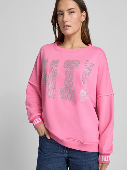 Frauenmodel trägt Sweatshirt mit Label-Detail von miss goodlife in Pink, reine Baumwolle, lockerer Schnitt, Nahaufnahme Oberkörper.