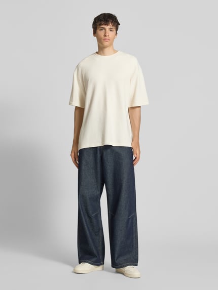 Männermodel trägt T-Shirt mit Strukturmuster und Rundhalsausschnitt Modell 'PETER' von Redefined Rebel, Relaxed Fit, helles Beige, Baumwoll-Mix, kombiniert mit weiter Jeans, Ganzkörperansicht von vorne.