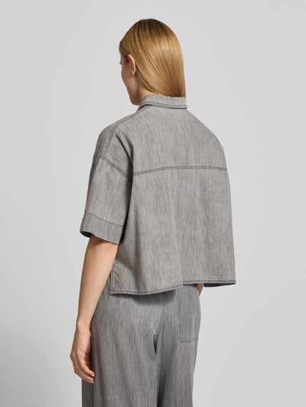 Kobiece modelka nosi bluzkę jeansową z bawełny, pudełkowy krój, model 'YARIKA' od Drykorn, kołnierzyk koszulowy, listwa guzikowa, długość tyłu 53 cm, długość rękawów 22 cm, widok całej sylwetki z tyłu.