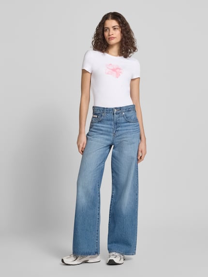Vrouwenmodel draagt Schmal geschnittenes T-Shirt aus Baumwollmix mit Blumen-Print van REVIEW, smal gesneden, ronde hals, bloemenprint, kort mouw, ruglengte bij maat S 54 cm, wit en roze, volledige lichaamsaanzicht van voren.