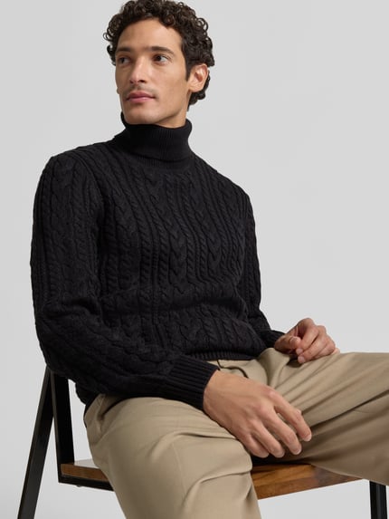 Męski model nosi Slim Fit Strickpullover mit Baumwoll-Anteil Modell 'Callum' od JACK & JONES Premium, czarny, melanż, warkoczowy wzór, długi rękaw, prążkowany golf i ściągacze, Ganzkörperansicht von vorne.