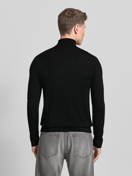 Männermodel trägt schwarzen Rollkragenpullover aus reiner Merinowolle Modell 'TRAY' von SELECTED HOMME, körpernaher Schnitt, Ganzkörperansicht Rückansicht.