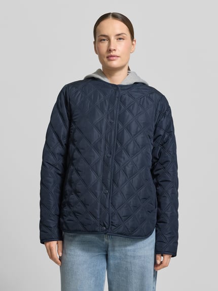Kobiece model prezentuje Regular Fit Jacke in Stepp-Optik mit Kapuze Modell 'Fenya' von Soyaconcept, kolor granatowy, z efektem pikowania, krój regular fit, kaptur, wpuszczane kieszenie, listwa guzikowa na całej długości, długość tyłu w rozmiarze S: 65 cm, szerokość ramion w rozmiarze S: 40 cm, szerokość w rozmiarze S: 54 cm, długość rękawów w rozmiarze S: 65 cm, widok całej sylwetki z przodu.