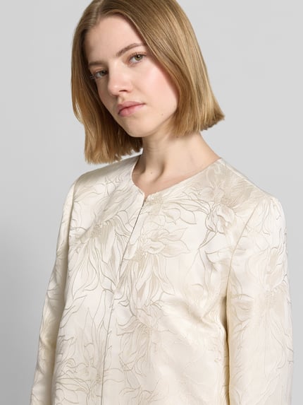 Vrouwenmodel draagt Blazer met Hakenverschluss Modell 'FULL' van EMME, recht model, ronde hals, crèmekleur met bloemmotief, detailopname bovenlichaam.