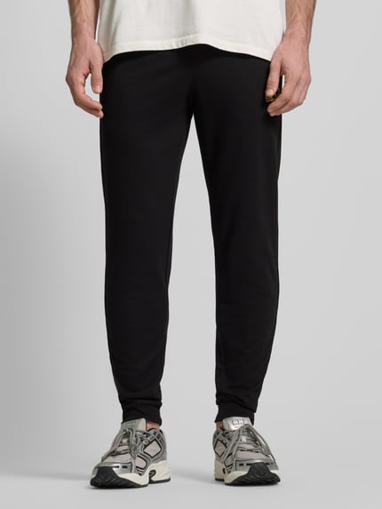 Männermodel trägt Sweatpants mit Logo und elastischem Bund von EA7 Emporio Armani, schwarze Farbe, Baumwoll-Elasthan-Mix, Ganzkörperansicht von vorne.