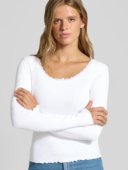 Frauenmodel trägt Longsleeve mit Spitzenbesatz und Rundhalsausschnitt von REVIEW, weiß, Ripp-Optik, Slim Fit, Nahaufnahme Oberkörper. Baumwoll-Elasthan-Mix, Rückenlänge bei Größe S: 50 cm.