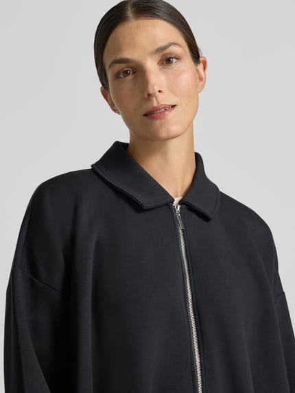 Frauenmodel trägt Sweatjacke mit Umlegekragen von Christian Berg Woman in Schwarz, glatte Textur, lockere Passform, Nahaufnahme Oberkörper, Modal-Mix, überschnittene Schultern, Reißverschluss, elastische Abschlüsse.