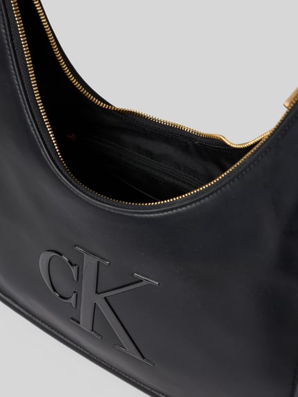 Productfoto, zwarte dames Henkeltasche met labeldetail van CK Calvin Klein, zichtbare logo in reliëf, goudkleurige ritssluiting, glad oppervlak