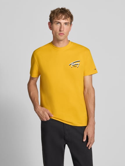 Männermodel trägt Regular Fit T-Shirt aus reiner Baumwolle von Tommy Jeans in Gelb mit kleinem Logo, Ganzkörperansicht von vorne.