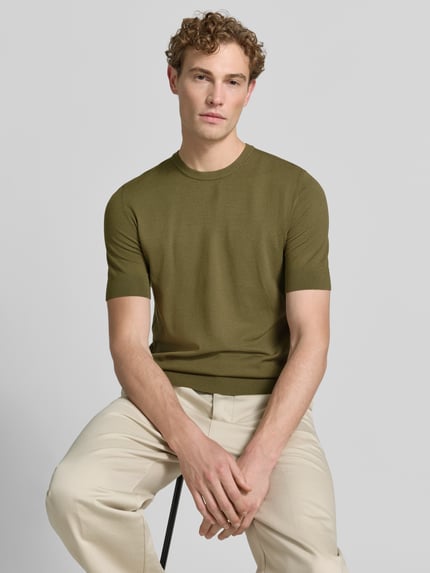 Męski model nosi Slim Fit T-Shirt aus Feinstrick model 'SAN CARL-CV' od HUGO w oliwkowym kolorze, gładka tekstura, zdjęcie w półzbliżeniu przód.