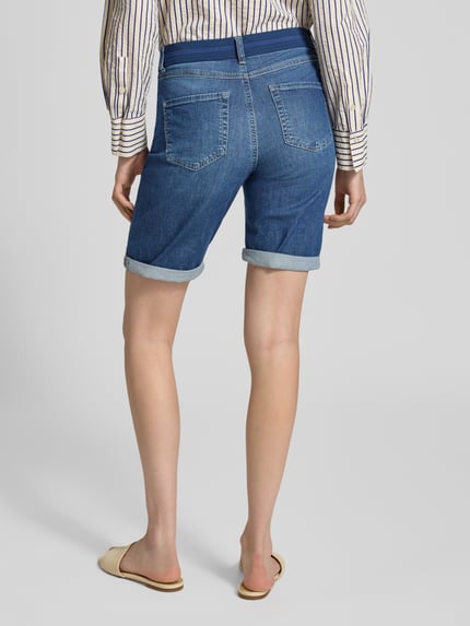 Frauenmodel trägt Jeansshorts mit Umschlag und elastischem Bund von Angels, blauer Baumwoll-Elasthan-Mix, Ganzkörperansicht Rückansicht.