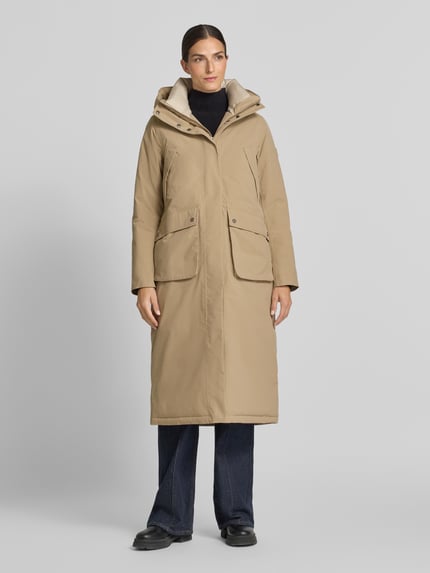 Frauenmodel trägt Regular Fit Parka mit Kapuze Modell 'Melody' von Didriksons in Beige, aufgesetzte Taschen, elastische Ärmelabschlüsse, Ganzkörperansicht von vorne. Rückenlänge, Schulterbreite, Brustweite, Ärmellänge entsprechend Größe 36.