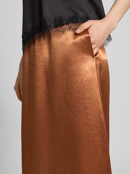 Vrouwenmodel draagt maxirok van glanzend koperkleurig satijn, A-lijn, model 'TUONO' van MM by Max Mara, detailopname heup.