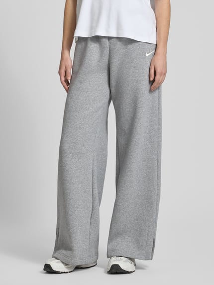 Frauenmodel trägt Loose Fit Sweatpants mit Logo-Stitching Modell 'Phoenix' von Nike aus Baumwoll-Mix in Grau, Nahaufnahme Unterkörper. Innenbeinlänge bei Größe M: 80 cm, Tunnelzug, für Damen.