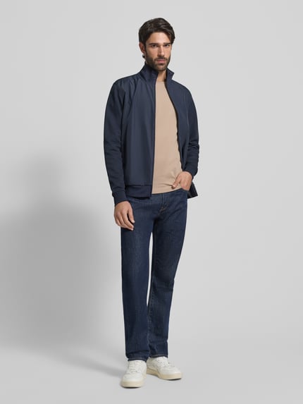 Männermodel trägt Regular Fit Blouson aus Baumwoll-Mix von Tommy Hilfiger in Dunkelblau, Stehkragen, Reißverschluss, Ganzkörperansicht von vorne.