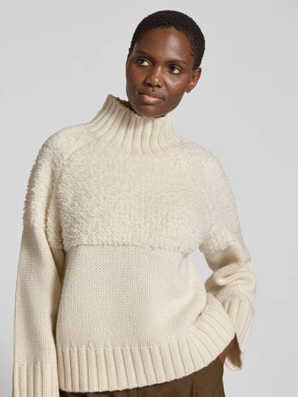 Frauenmodel trägt Pullover mit Teddystruktur Modell 'ROTHLEY' von BARBOUR in Creme, Strickoptik, Strukturmuster, Mock Neck, Raglanärmel, Rippstrickdetails, Ganzkörperansicht von vorne.