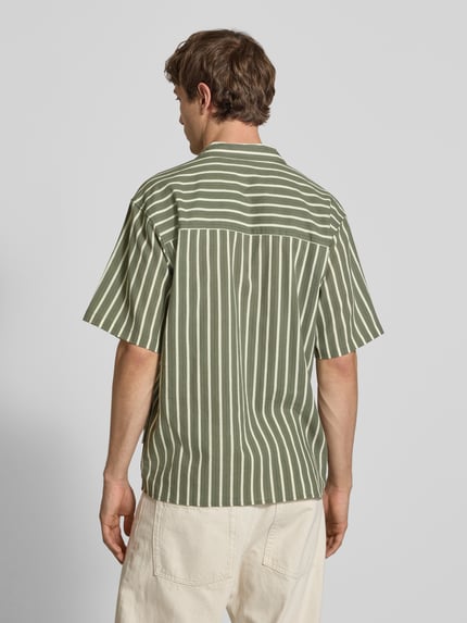 Männermodel trägt Regular Fit Freizeithemd mit Reverskragen Modell 'HOWIE' von Redefined Rebel, Reine Baumwolle, Allover-Look, Label-Detail, Ganzkörperansicht Rückansicht. Rückenlänge bei Größe M 60 cm, Schulterbreite 60 cm, Ärmellänge 30 cm. Beige Hose, grün-weiß gestreiftes Hemd, glatte Textur.