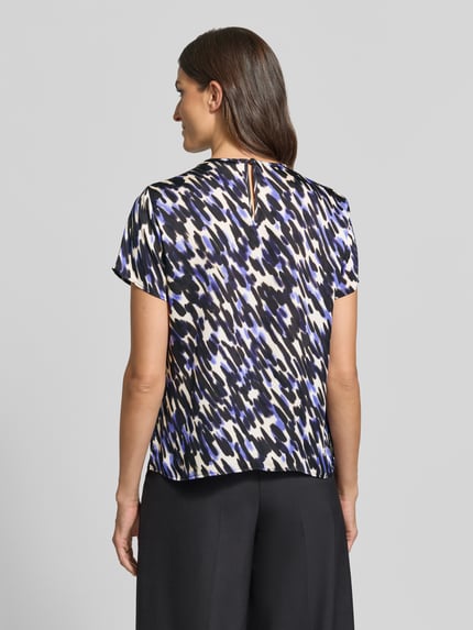 Kobiece modelka ma na sobie bluzkę z krótkim rękawem Regular Fit Kurzarmbluse mit Falten-Detail od s.Oliver BLACK LABEL, wzór w czerni, bieli i fiolecie, gładka tekstura, widok całej sylwetki z tyłu.