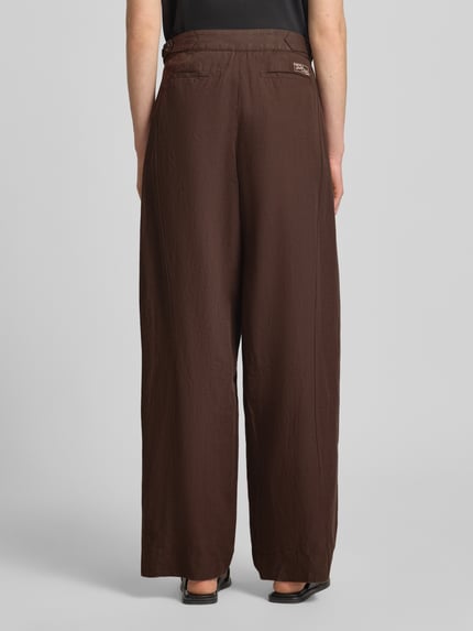 Frauenmodel trägt Wide Leg Hose mit Eingrifftaschen Modell 'QUINN' von Scotch & Soda in Braun, Baumwoll-Leinen-Mix, Ganzkörperansicht Rückansicht.