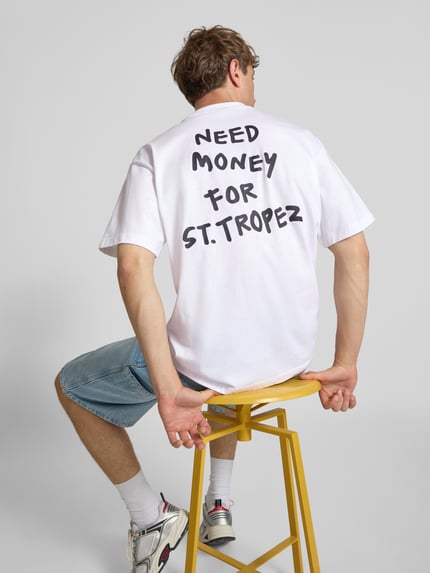 Męski model nosi Loose Fit T-Shirt aus reiner Baumwolle Modell 'MONEY' von Only & Sons w jednolitym białym kolorze z czarnym nadrukiem statement, okrągły dekolt, krótki rękaw, gładka dzianina jersey, widok całej sylwetki z tyłu