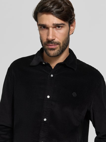 Männermodel trägt Regular Fit Freizeithemd mit Label-Stitching von MCNEAL, schwarze Baumwolle, Cord, Kentkragen, Nahaufnahme Oberkörper.