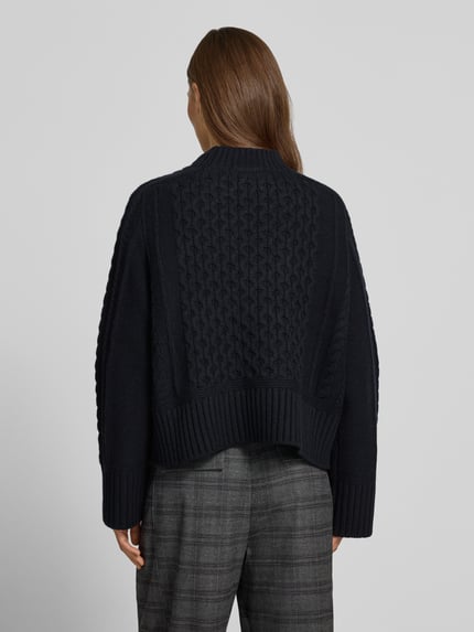 Frauenmodel trägt Strickpullover mit Zopfmuster von Style Icon Collection, dunkle Farbe, lockere Passform, Ganzkörperansicht Rückansicht. Reine Baumwolle, Rundhalsausschnitt, gerippte Abschlüsse, Rückenlänge 46 cm, Ärmellänge 71 cm.