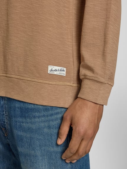Männermodel trägt Regular Fit Sweatshirt mit Rundhalsausschnitt von Scotch & Soda, katoenmix, labeldetail, detailaufnahme rechter onderarm