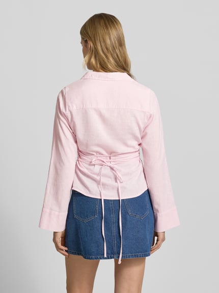 Frauenmodel trägt Leinenbluse mit Bindegürtel und V-Ausschnitt von Gina Tricot im zarten Rosa, Leinen-Baumwoll-Anteil, taillierter Schnitt, Kentkragen, Knopfleiste, Rückansicht, Ganzkörperansicht.