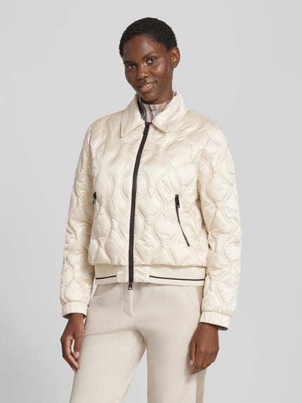 Frauenmodel trägt Steppjacke mit Umlegekragen und Reißverschlusstaschen von Marc Cain in Beige, strukturierte Oberfläche, Regular Fit, Ganzkörperansicht von vorne. Rückenlänge 56 cm, Schulterbreite 45 cm, Brustweite 58 cm, Ärmellänge 61 cm.