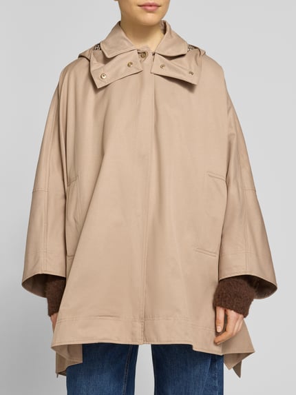 Frauenmodel trägt Cape mit Kimonoärmeln und Kapuze von Stefanel in Beige, Baumwoll-Mix, verdeckter Reißverschluss, Nahaufnahme Oberkörper.
