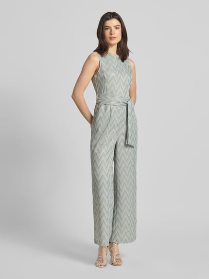 Vrouwenmodel draagt Regular Fit Jumpsuit met geometrisch all-over stitching van Betty Barclay in lichtgrijs en beige, getailleerde pasvorm, afneembare stoffen band, mouwloos design, boothals, ruglengte maat 36: 141 cm, borstwijdte maat 36: 32 cm, totale lengte maat 36: 141 cm, binnenbeenlengte: 73 cm, volledig zicht van voren.