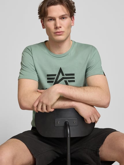 Männermodel trägt T-Shirt mit Logo und Rundhalsausschnitt von Alpha Industries in Mintgrün, reine Baumwolle, Regular Fit, Nahaufnahme Oberkörper.
