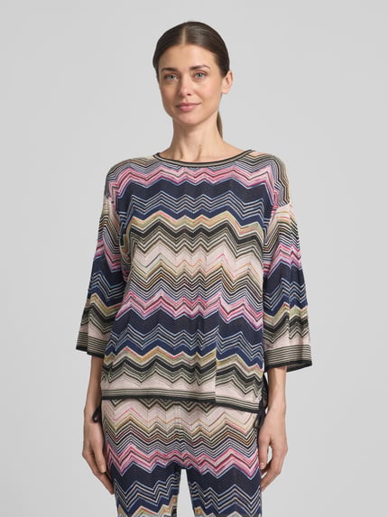 Kobiece modelka nosi Strickshirt mit 3/4-Arm od Oui, mieszanka wiskozy i bawełny, krój regular fit, wzór na całej powierzchni, okrągły dekolt, rękaw o dł. 3/4, długość tyłu w rozmiarze 36: 57 cm, długość rękawów w rozmiarze 36: 36 cm, kolorowe zygzakowate wzory, tekstura dzianiny, widok na całą sylwetkę z przodu.