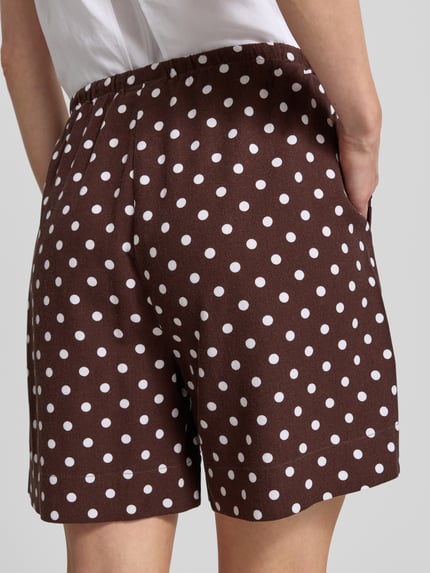 Vrouwenmodel draagt korte broek model 'Lavisco' van FREE/QUENT, viscosemix met linnen en rechte pasvorm, bruine stof met witte stippen, tunnelkoord. Ganzkörperaanzicht achteraan, bandwijdte maat S 42 cm, binnenbeenlengte maat S 16 cm.