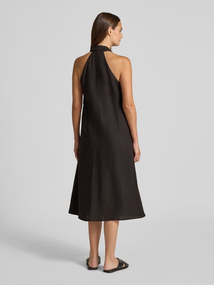Frauenmodel trägt Midikleid aus Viskose-Mix mit Neckholder Modell 'Qudia' von Someday in Schwarz, Rückenansicht, Loose-Fit, glatte strukturierte Oberfläche, Damen Midikleid mit Leinen-Viskose-Anteil, Nahtreißverschluss, Rückenlänge 116 cm, Brustweite 48 cm, Ganzkörperansicht Rückansicht.