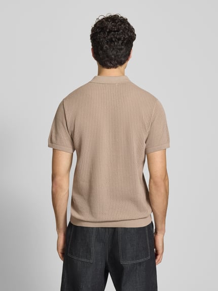 Männermodel trägt Modern Fit Poloshirt mit kurzer Knopfleiste Modell 'JESS' von Jack & Jones aus Baumwoll-Mix, semitransparentes Design, beige Farbe, Polokragen, strukturierte Textur, Ganzkörperansicht Rückansicht.