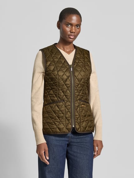 Frauenmodel trägt Regular Fit Weste mit V-Ausschnitt Modell 'BETTY' von Barbour in Olivgrün, gesteppte Struktur, Ganzkörperansicht von vorne. Damen Weste von Barbour.