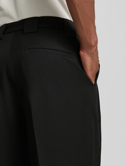 Männermodel trägt Stoffhose mit Bügelfalten und Eingrifftaschen von MCNEAL aus schwarzem Material-Mix mit Viskose-Anteil, Detailaufnahme.